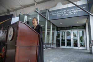 Ruby DeChristofaro stands at a podium in front of the Joseph and Ruby DeChristofaro Center for Biotechnology and Life Sciences.